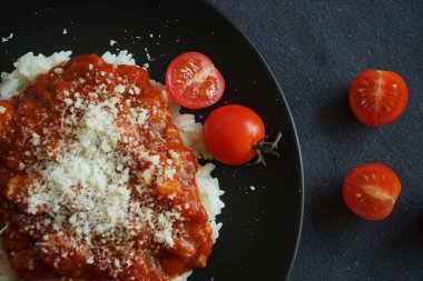 Domates soslu pilav, köfte ve siyah tabakta parmesan peyniri yanında çatal ve kiraz domatesli gri masa örtüsü.