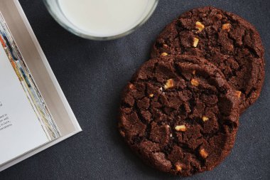 Gri bir masada bir bardak sütle çikolatalı kurabiyeler.