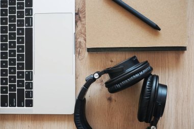 Siyah kulaklıklar, not defterleri ve ahşap bir masada yan yana açık bir laptop.