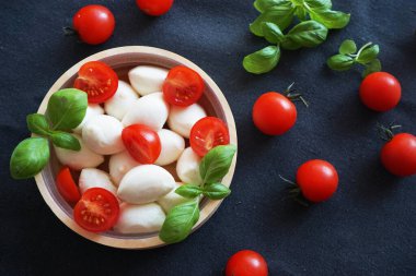 Koyu gri arka planda fesleğenli kiraz domatesli Mozzarella.