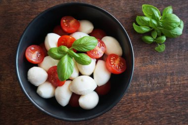 Tahtada fesleğenli siyah bir tabakta kiraz domatesli Mozzarella.