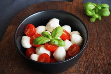 Tahtada fesleğenli siyah bir tabakta kiraz domatesli Mozzarella.
