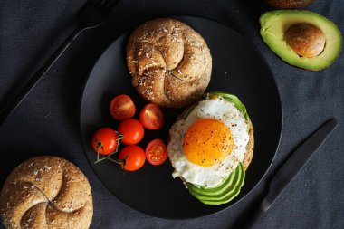 Yağda yumurta, avokado, siyah arka planda siyah bir tabakta ekmekli kiraz domatesleri.