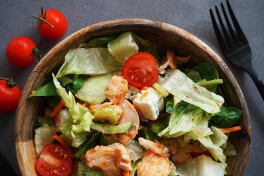 Gri arka planda çatal ve bıçağın yanında tavuk ve peynirli sebze salatası.