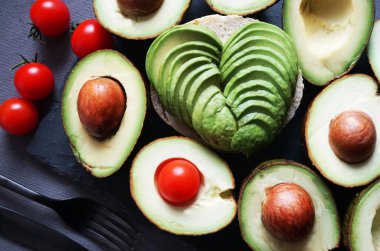 Çeri domateslerinin, çatalın ve bıçağın yanında bir sürü dilimlenmiş avokado var.