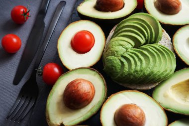 Çeri domateslerinin, çatalın ve bıçağın yanında bir sürü dilimlenmiş avokado var.