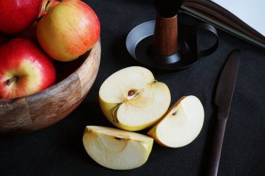 Diğer elmaların yanında kesilmiş bir elma, bir kitap, bir şamdan ve siyah bir arka planda bir bıçak.