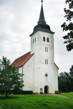 Çimlerin ve ağaçların arkasındaki eski beyaz taş kilise.