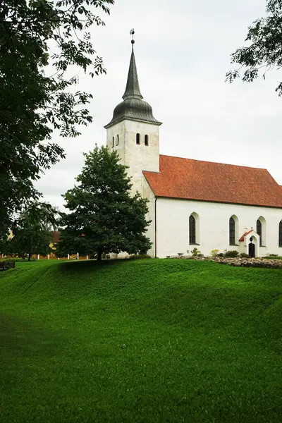 Çimlerin ve ağaçların arkasındaki eski beyaz taş kilise.