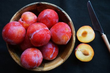 Dilimlenmiş eriklerin yanında olgun erikler ve koyu bir masa örtüsünün üzerinde bir bıçak.