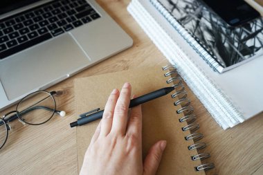 Not defterlerinin arka planında bir kalem, gözlüklü bir akıllı telefon, ahşap bir masada açık bir dizüstü bilgisayar.