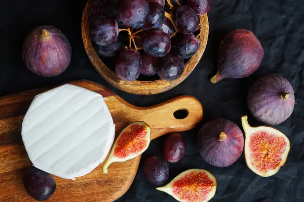 Camembert peyniri, olgun incir, koyu arkaplanda kırmızı üzüm.