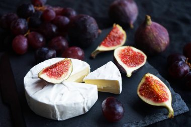 Olgun incir, Camembert peynirli kırmızı üzüm ve koyu arkaplanda çatal bıçak takımı.