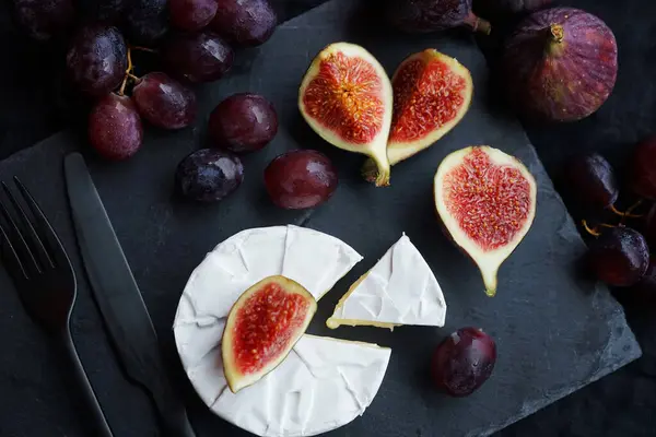 Olgun incir, Camembert peynirli kırmızı üzüm ve koyu arkaplanda çatal bıçak takımı.