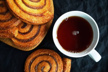 Tarçınlı ruloların yanında koyu arkaplanda bir fincan çay