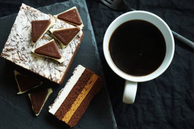 Çikolatalı kek, çikolata parçalarının yanında ve arka planda bir fincan kahve.