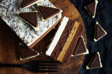Koyu bir arka planda, tahta bir standın üzerinde çikolata parçalarının yanında çikolatalı pasta.