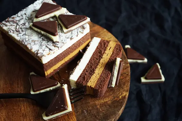 Koyu bir arka planda, tahta bir standın üzerinde çikolata parçalarının yanında çikolatalı pasta.