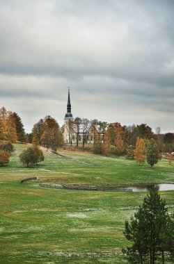 Yeşil çayır, sonbahar ormanı ve kasvetli gökyüzü karşısında eski bir Protestan kilisesi.