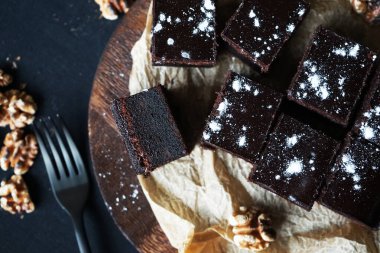 Cevizlerin yanında çikolatalı brownie ve siyah bir arka planda tahta bir çatal.