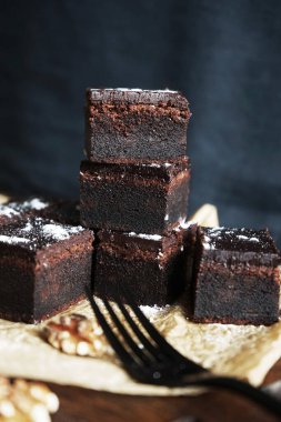 Cevizlerin yanında çikolatalı brownie ve siyah bir arka planda tahta bir çatal.