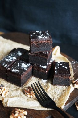 Cevizlerin yanında çikolatalı brownie ve siyah bir arka planda tahta bir çatal.