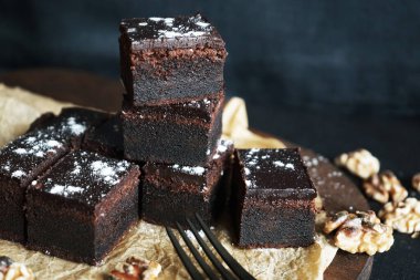 Cevizlerin yanında çikolatalı brownie ve siyah bir arka planda tahta bir çatal.