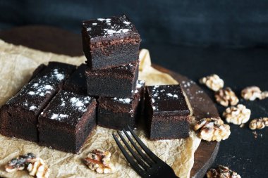 Cevizlerin yanında çikolatalı brownie ve siyah bir arka planda tahta bir çatal.