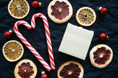 Kurumuş narenciye meyvelerinin yanında iki kalp şeklinde şeker kamışı, Noel ağacı süslemeleri ve notlar için bir not defteri.