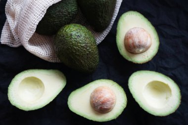 Koyu arkaplanda diğer avokadoların yanında olgun avokadoyu kes