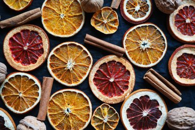 Kuru portakal ve tarçın yanında greyfurt dilimleri ve koyu bir arka planda ceviz.