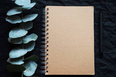 Karanlık bir arkaplanda okaliptüs dalının yanındaki not defterinde.