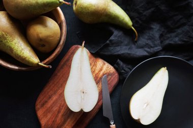 Tam ve dilimlenmiş armutlar tahtada ve tabaklarda koyu bir zemin üzerinde.