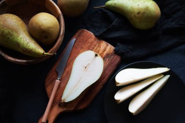 Tam ve dilimlenmiş armutlar tahtada ve tabaklarda koyu bir zemin üzerinde.