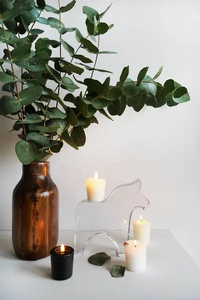 Eucalyptus branches in a wooden vase next to candles on a light background