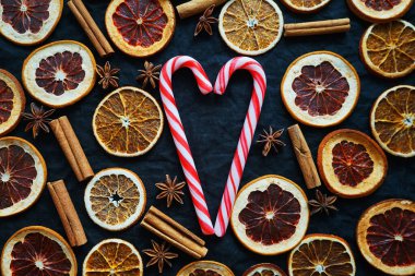 Kuru narenciye dilimleri, tarçın ve yıldız anasonunun yanında kalp şeklinde baston şekerler.