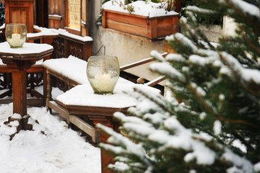 Cam bir şamdanda yanan bir mum, dışarıda, ahşap bir masada, bir Noel ağacının arka planında.