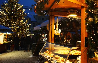 Noel ağacının arka planında farklı tabak ve sosislerle ahşap tezgah ve kış akşamları insanlar.
