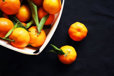Siyah arka planda bir kutu mandalinanın yanında bütün mandalina var.