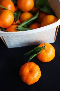 Siyah arka planda bir kutu mandalinanın yanında bütün mandalina var.