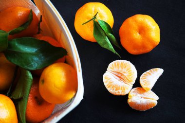 Siyah arka planda bir kutu mandalinanın yanında parçalar ve mandalinalar var.