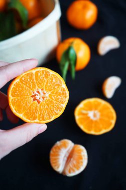 Siyah arka planda bir kutu mandalinanın yanında parçalar ve mandalinalar var.