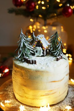 Beyaz kremalı, zencefilli kek ve Noel ışıklarının arka planında köknar ağaçları.