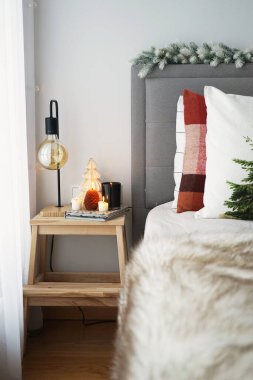 Yastıklı ve battaniyeli bir yatağın yanında lamba ve mumlarla komodin.