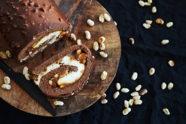 Çikolata rulo krema ve karamel yanında yer fıstığı. Tahta tepside, karanlık bir arka planda.