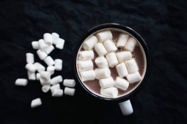 Bir fincan marşmelovlu kakao, siyah arka planda beyaz şekerlemelerin saçıldığı yerde.