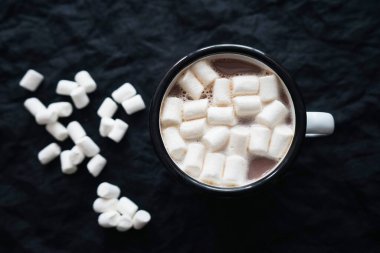 Bir fincan marşmelovlu kakao, siyah arka planda beyaz şekerlemelerin saçıldığı yerde.