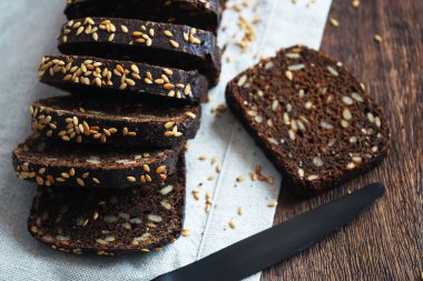 Keten peçetede siyah bir bıçağın yanında dilimlenmiş siyah ekmek.