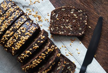 Keten peçetede siyah bir bıçağın yanında dilimlenmiş siyah ekmek.