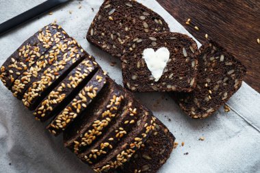 Dilimlenmiş ekmeğin yanında tereyağlı bir kalp ve keten peçetede bir bıçak olan bir parça siyah ekmek.